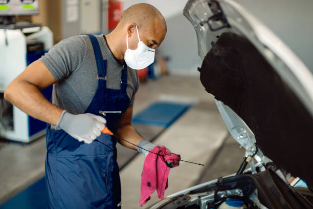 African American repairman wearing protective face mask and examining car oil in a workshop.